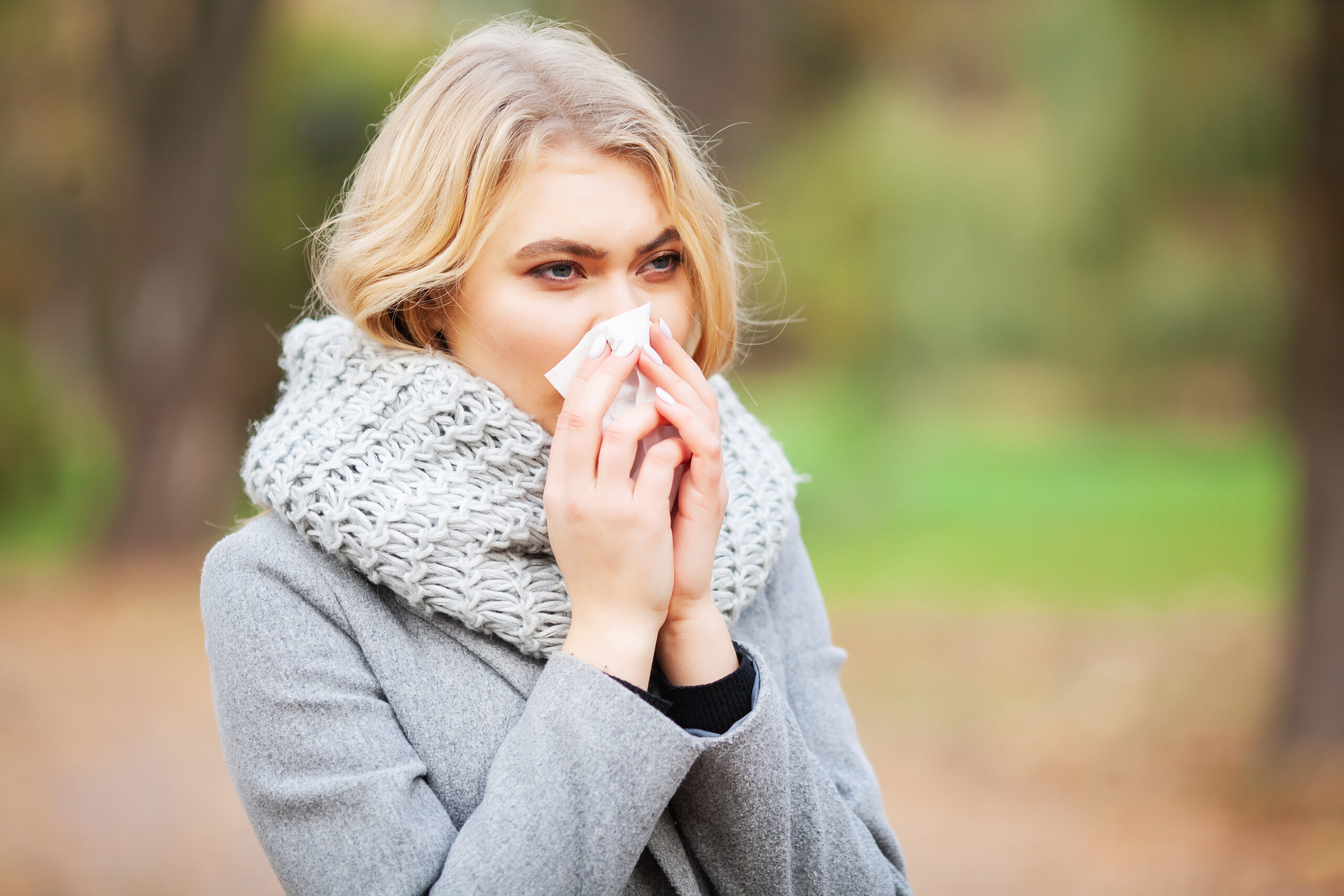 Lady outside during fall suffering from a runny nose, a common symptom of the common cold and flu.